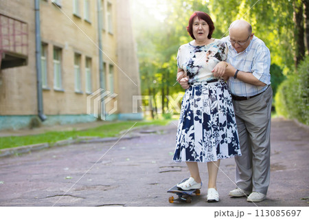Happy elderly couple with a skateboard. Handsome man and woman senior citizens. Husband and wife of old age for a walk in the city. 113085697