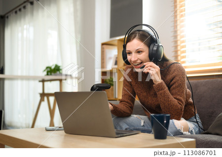 Cheerful young woman wearing headset playing video game with joystick in at home Cheerful young woman wearing headset playing video game with joystick in at home 113086701
