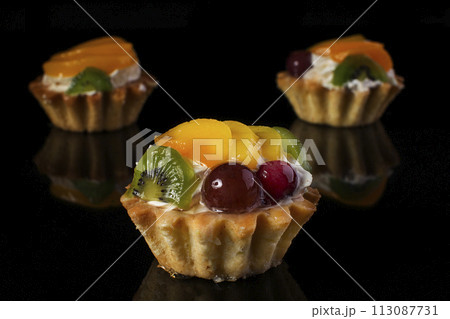 cake basket with kiwi fruit peach gooseberries close-up on a black background 113087731