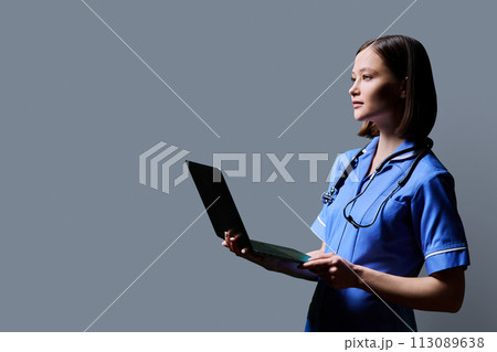 Female nurse using laptop, profile view on gray studio background 113089638