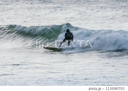 Experienced surfer surfing a wave alone on the beach in winter with wetsuit on 113090701