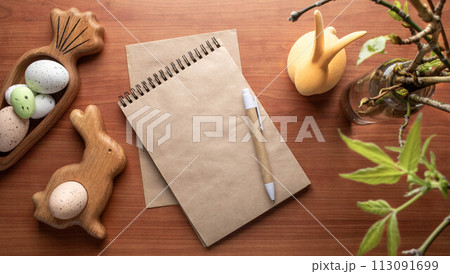 Blank notepad, pen, Easter figured wooden plates with eggs, spring twigs on wooden desk. Top view. 113091699