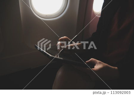 Blonde female tourist checking incoming notification on smartphone sitting on seat of airplane with netbook.Young businesswoman share media from telephone on laptop computer during plane flight 113092003