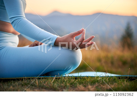 Close up of woman's hands on dawn background in the evening. Woman doing yoga exercise and meditating during sunset in mountains 113092362