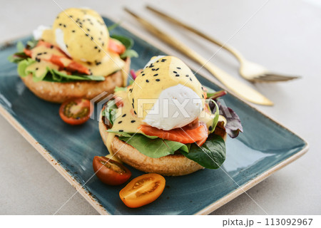 Eggs Benedict with salad leafs, salmon and fresh cherry tomato 113092967