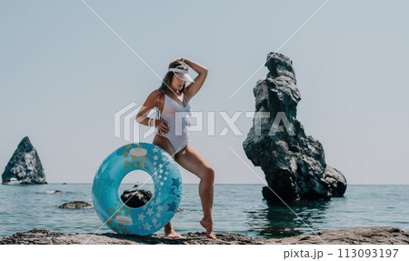 Woman summer sea. Happy woman swimming with inflatable donut on the beach in summer sunny day, surrounded by volcanic mountains. Summer vacation concept. Woman summer sea. Happy woman swimming with inflatable donut on the beach in summer sunny day, surrounded by volcanic mountains. Summer vacation concept. 113093197