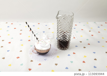 cup of coffee with whipped cream and sprinkles next to a vintage fake crystal decanter 113093944