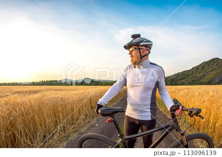 the cyclist with the bike in a field watching the sunset. sports and hobbies. outdoor activities the cyclist with the bike in a field watching the sunset. sports and hobbies. outdoor activities 113096139