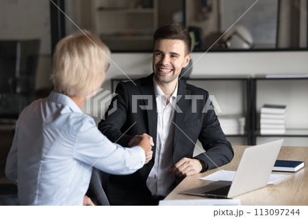 Cheerful professional man shaking hands with mature colleague woman Cheerful professional man shaking hands with mature colleague woman 113097244