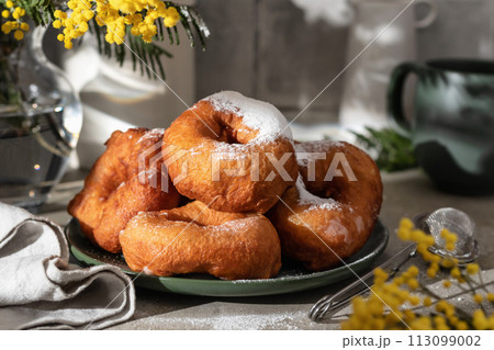 Delicious homemade crumpets or fried donuts sprinkled with powdered sugar on gray tile kitchen background in hard light 113099002