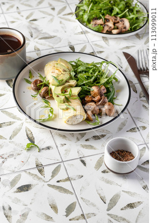 French rolled omelette stuffed with cream cheese with avocado, aragula and mushrooms for breakfast on white plate printed tile background, text space French rolled omelette stuffed with cream cheese with avocado, aragula and mushrooms for breakfast on white plate printed tile background, text space 113099011