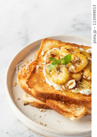 Sweet toast with cream cheese, caramelized banana, nuts and honey in white plate on marble background, close up, text space Sweet toast with cream cheese, caramelized banana, nuts and honey in white plate on marble background, close up, text space 113099013