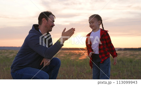 Daughter father special handshake greeting clapping hands gesture expressing strong close family relationship. Baby girl kid child man dad at sunset sunrise in field happy relatives hugging cuddling. 113099943