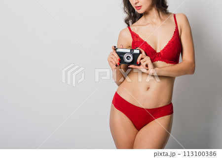 Beautiful female with pretty smile in red lingerie holding photo camera, isolated on white 113100386