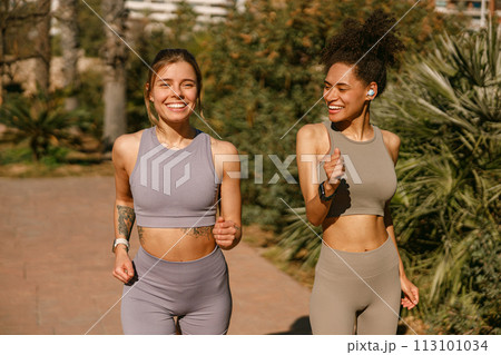 Two active women athlete running side by side along an outdoor track on public park background 113101034