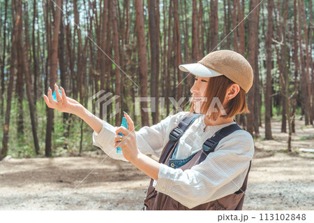 キャンプ場で虫除けスプレー・日焼け止めスプレーを使う女性 キャンプ場で虫除けスプレー・日焼け止めスプレーを使う女性 113102848