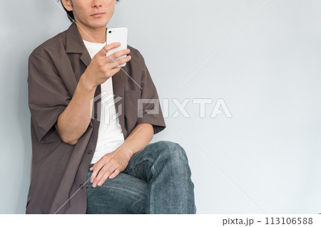 スマホを使う若いアジア人男性（ストレートネック・巻き肩・猫背・ドライアイ・スマホ老眼・眼精疲労） 113106588
