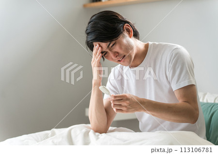 ベッドで体温を測る体調不良の男性（熱・風邪・頭痛・だるい） 113106781
