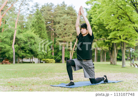 公園でヨガマットをひいてヨガ・ピラティスをする若い男性 113107748