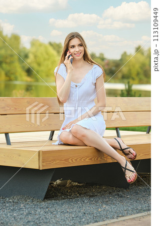 Satisfied woman calls her friend and invites her for walk in city park 113109449