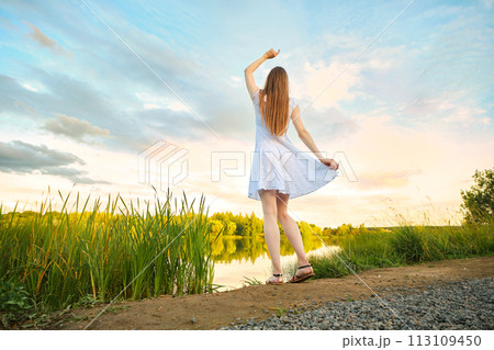 Young woman enjoying sunset standing by the river bank 113109450