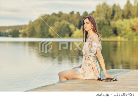 Young woman sits on the pier by the river 113109455