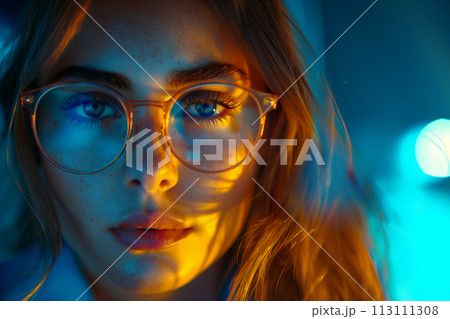 Mid shot portrait of female student with glasses looking at camera, neon lighting in computer lab, concept of importance of education 113111308