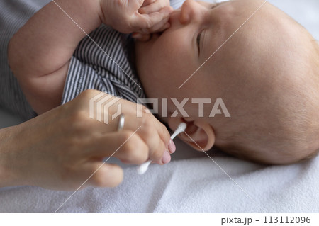 Female hand with wrong cotton swab near ear of a baby. Dangerous ears cleaning of the babies. Female hand with wrong cotton swab near ear of a baby. Dangerous ears cleaning of the babies. 113112096