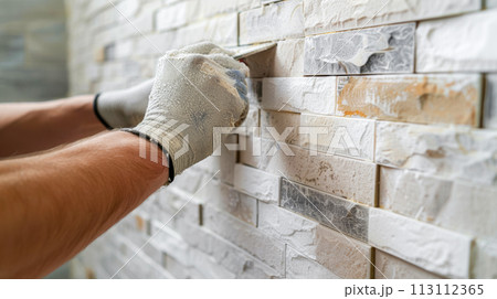 Renovation of apartments and offices, a specialist applies a fugue with a spatula to the seams between artificial stone on the wall, close-up, advertising concept for construction crews 113112365