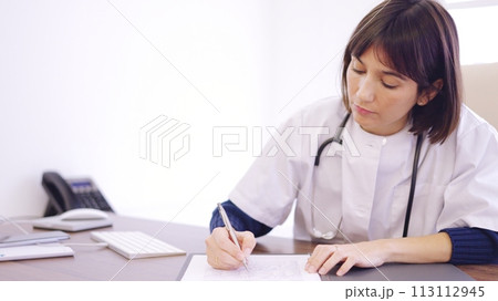 Female doctor filling a report sitting on a clinic Female doctor filling a report sitting on a clinic 113112945