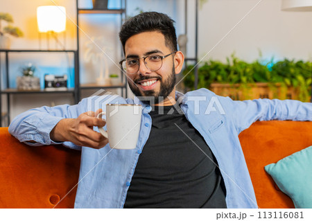 Tired smiling Indian man drinking cup of warm coffee or herbal tea in the morning relaxing enjoying 113116081