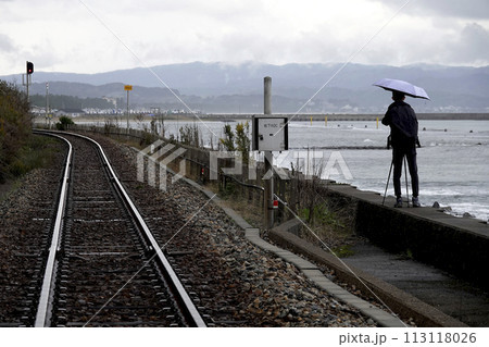 海岸線に敷かれたローカル鉄道の線路と撮影者のシルエット 113118026