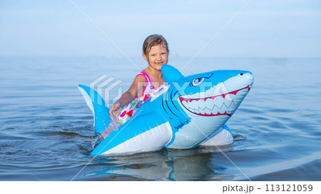 Happy girl swimming on an inflatable shark toy in the sea 113121059