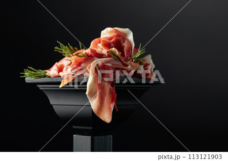 Prosciutto with rosemary on a black podium. 113121903