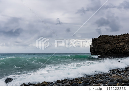 Surf on a rocky coast in front of the horizon under a cloudy sky. Tropical stormy ocean with waves crashing on the rocks. Stormy sea with stormy clouds and black lava rocks on the shore. Splashing Surf on a rocky coast in front of the horizon under a cloudy sky. Tropical stormy ocean with waves crashing on the rocks. Stormy sea with stormy clouds and black lava rocks on the shore. Splashing 113122288