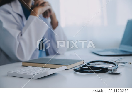 Doctor and patient sitting at the desk in clinic office. The focus is on female physician's hands filling up the medication history record form, close up. Medicine concept Doctor and patient sitting at the desk in clinic office. The focus is on female physician's hands filling up the medication history record form, close up. Medicine concept 113123252