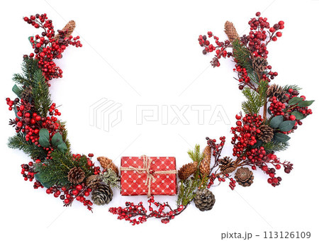 Christmas composition on isolated white background. New year wrapped gift, pine cones, thuja or fir branches and red berries on snow. Top view, flat lay, copy space. Circular shape. Decor for design. 113126109
