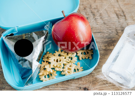 Asian student's lunchbox of onigiri,chips and apple with bottle of water,On wooden background Asian student's lunchbox of onigiri,chips and apple with bottle of water,On wooden background 113126577