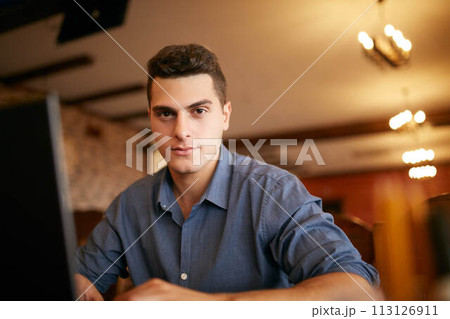 Authentic portrait of young confident businessman looking at camera with laptop in office. Hipster man and knitted sweater doing his startup ICO project. Smart casual wear. Business theme Authentic portrait of young confident businessman looking at camera with laptop in office. Hipster man and knitted sweater doing his startup ICO project. Smart casual wear. Business theme 113126911