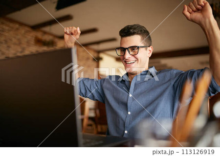 Handsome businessman with laptop having his arms with fists raised, celebrating success. Happy freelancer hipster in glasses finished work on project. Man won a lot of money in lottery prize. Handsome businessman with laptop having his arms with fists raised, celebrating success. Happy freelancer hipster in glasses finished work on project. Man won a lot of money in lottery prize. 113126919