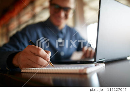Close-up of smiling man hand writing on paper notebook. Young businessman in glasses taking notes in notepad with stylish premium fountain pen. Male signing contract. Student working on laptop. 113127045