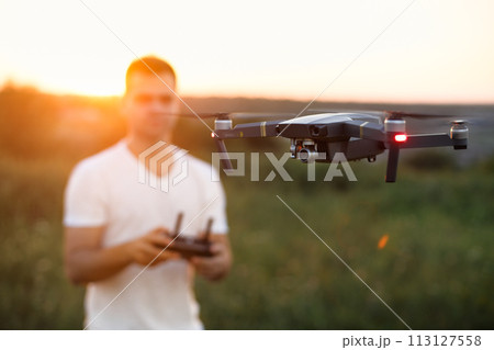 Drone hovers in front of man with remote controller in his hands. Quadcopter flies near pilot. Guy taking aerial photos and videos from above 113127558