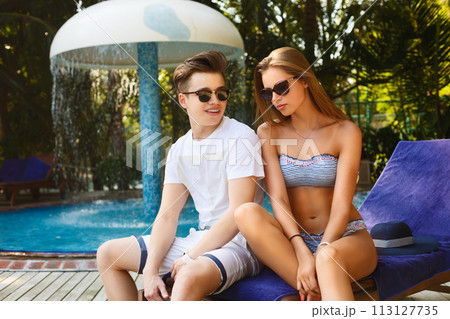 Spending carefree time poolside. Happy couple holding cocktails and smiling while sitting at the deck chairs by the pool. Vacation concept 113127735