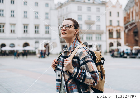 Tourist happy woman in glasses on Market Square in Krakow, Traveling Europe in autumn. St. Marys Basilica, cloudy day Tourist happy woman in glasses on Market Square in Krakow, Traveling Europe in autumn. St. Marys Basilica, cloudy day 113127797
