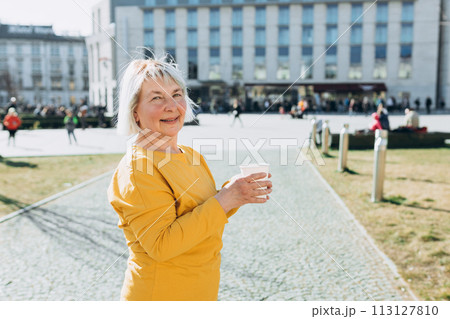 Happy mature caucasian woman in good mood walks with coffee around city during day. Lifestyle concept. Senior holding takeaway coffee cup on urban background Happy mature caucasian woman in good mood walks with coffee around city during day. Lifestyle concept. Senior holding takeaway coffee cup on urban background 113127810