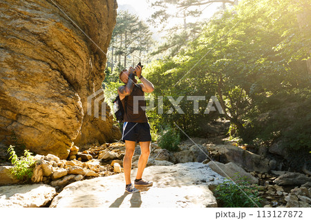 Bearded photographer man trekking among forest and mountains and taking pictures with dslr camera. Horizontal shape, copy space Bearded photographer man trekking among forest and mountains and taking pictures with dslr camera. Horizontal shape, copy space 113127872
