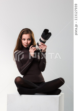 The beautiful photographer girl with professional dslr camera posing on a white background in studio. Photo learning, studying, training concept The beautiful photographer girl with professional dslr camera posing on a white background in studio. Photo learning, studying, training concept 113127939