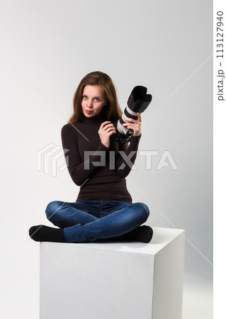 The beautiful photographer girl with professional dslr camera posing on a white background in studio. Photo learning, studying, training concept The beautiful photographer girl with professional dslr camera posing on a white background in studio. Photo learning, studying, training concept 113127940