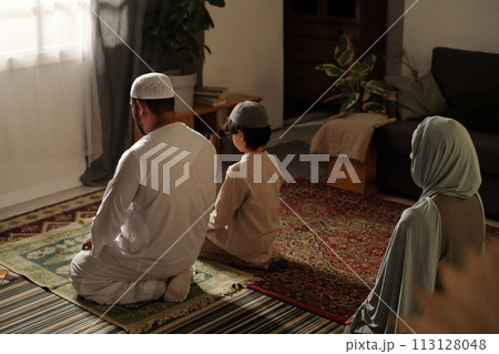 High angle view of unrecognizable Muslim family with kid sitting on floor in living room praying salah High angle view of unrecognizable Muslim family with kid sitting on floor in living room praying salah 113128048