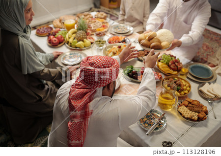High angle view of young Muslim man sharing food with his family at festive dinner on Uraza Bayram High angle view of young Muslim man sharing food with his family at festive dinner on Uraza Bayram 113128196